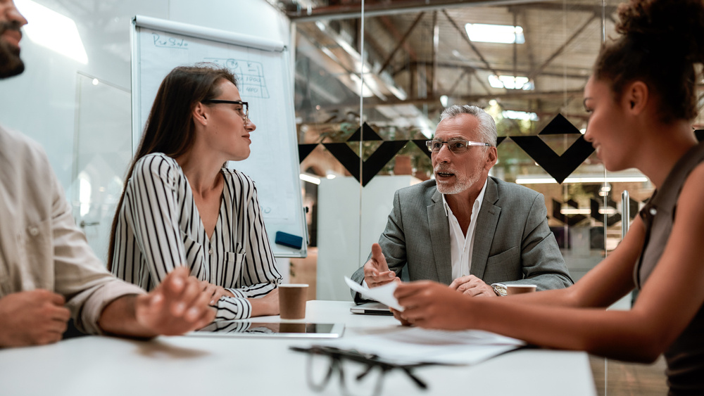 A diverse group of employees engaged in a team feedback session in a modern office setting.